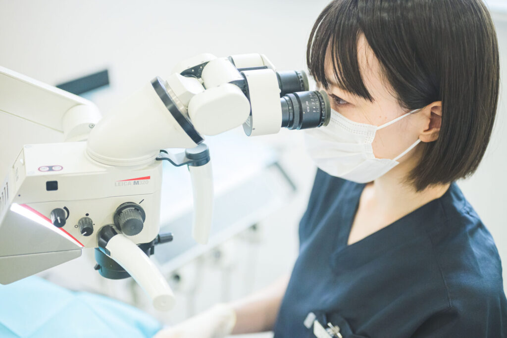 愛媛インプラントクリニックかまくら歯科にて、歯科医師がLEICA（ライカ）社製のマイクロスコープ（歯科用顕微鏡）を用いて精密な治療を行っている様子。肉眼では見えない細かな虫歯や歯の根の管を確認し、インプラント治療や根管治療の精度を高めるための高度な設備を使用しています。