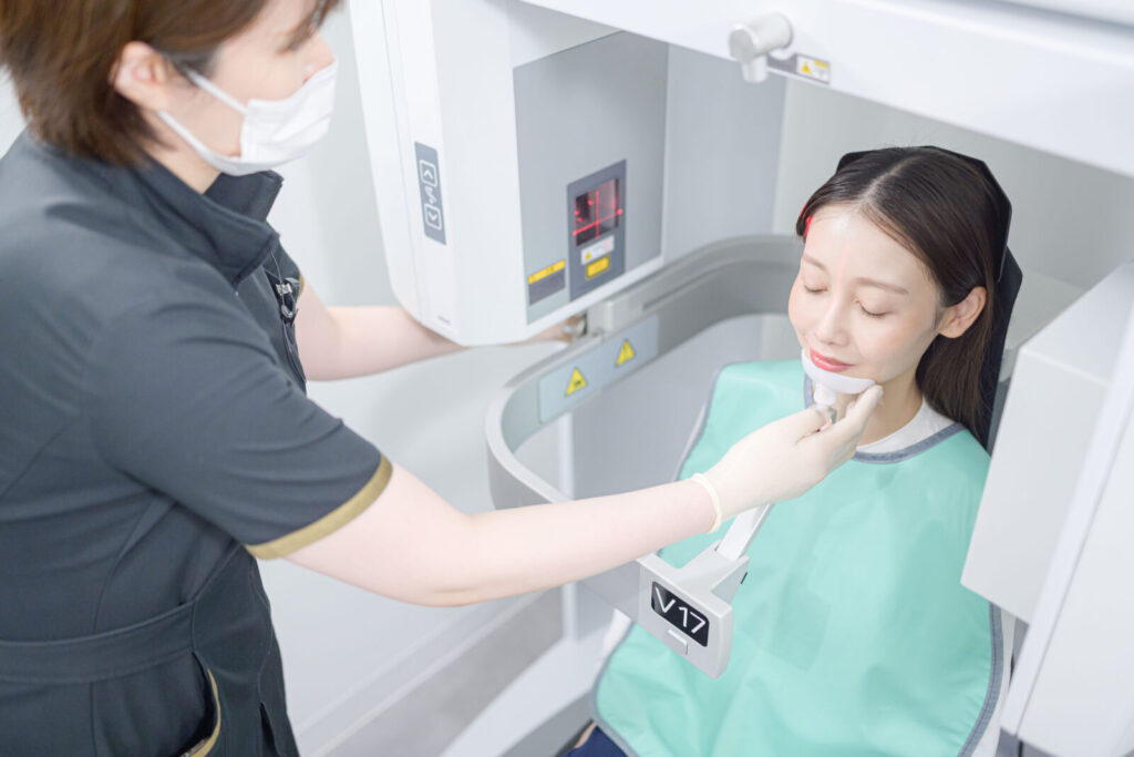 愛媛インプラントクリニックかまくら歯科にて、インプラント治療の精密検査（歯科用CT撮影）を行う様子。歯科スタッフが患者様の顎の位置を丁寧に調整し、安全かつ正確な診断のためのデータを取得しています。愛媛県松山市で最先端の医療機器を用いた精密な歯科診療を提供しています。