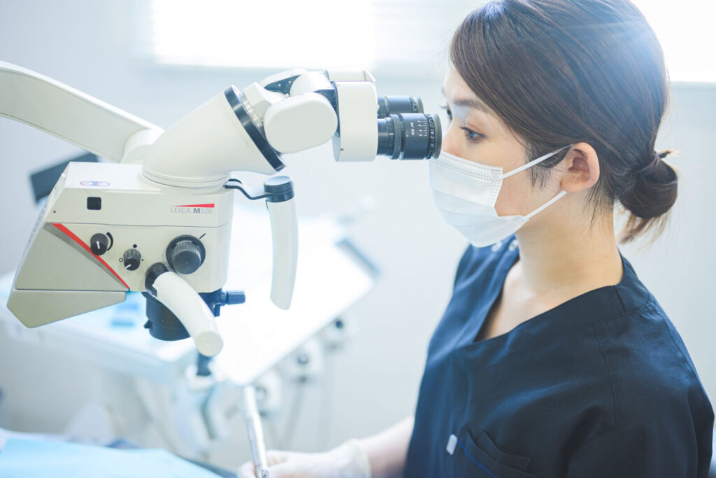 愛媛インプラントクリニックかまくら歯科にて、歯科医師がマイクロスコープ（歯科用顕微鏡）を使用して精密な根管治療（歯の根の治療）を行っている様子。肉眼では見えない細かな患部を強拡大し、再発リスクを抑えた高度な歯科診療を愛媛県松山市で提供しています。